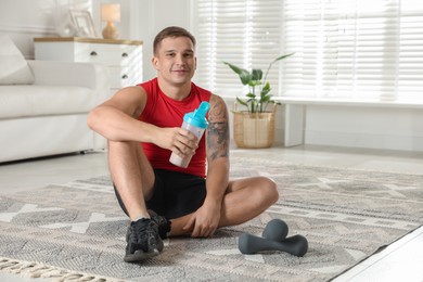 Photo of Athletic man with shaker of protein drink sitting on carpet at home