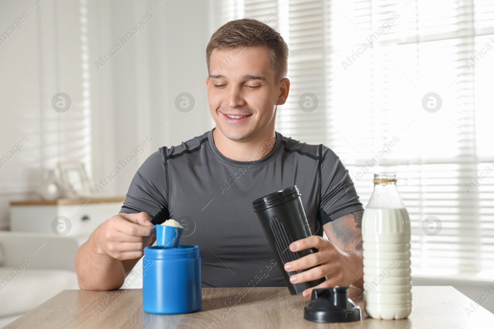 Photo of Making protein cocktail. Smiling man with scoop of powder and shaker at wooden table