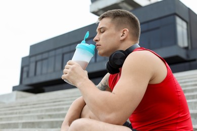 Photo of Athletic man drinking protein shake outdoors, low angle view. Space for text