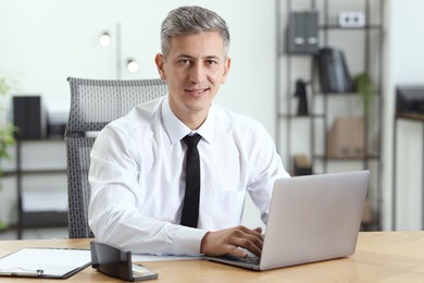 Photo of Businessman working on laptop at table in office