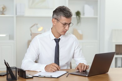 Photo of Businessman working on laptop at table in office