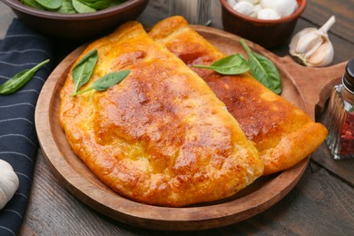 Photo of Tasty calzones with basil served on wooden table, closeup