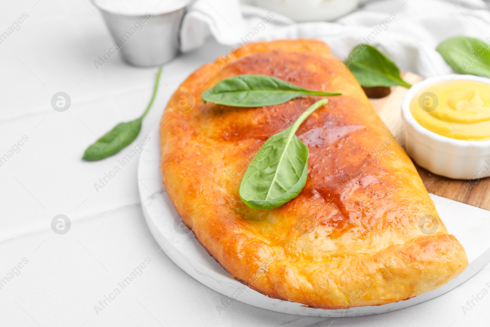 Photo of Tasty calzone with basil and sauce on white table, closeup. Space for text