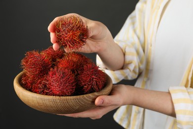 Photo of Woman holding fresh rambutans in bowl on black background, closeup