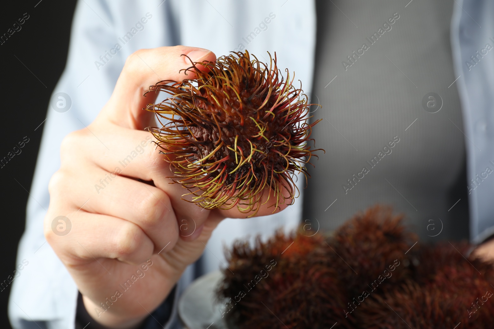 Photo of Woman holding fresh rambutans on plate against black background, closeup