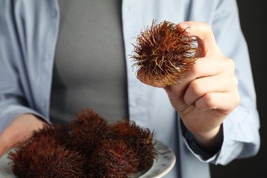 Photo of Woman holding fresh rambutans on plate against black background, closeup