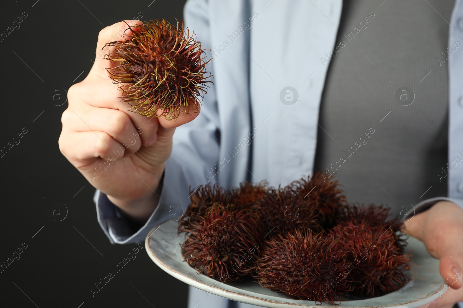 Photo of Woman holding fresh rambutans on plate against black background, closeup