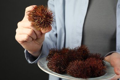 Woman holding fresh rambutans on plate against black background, closeup