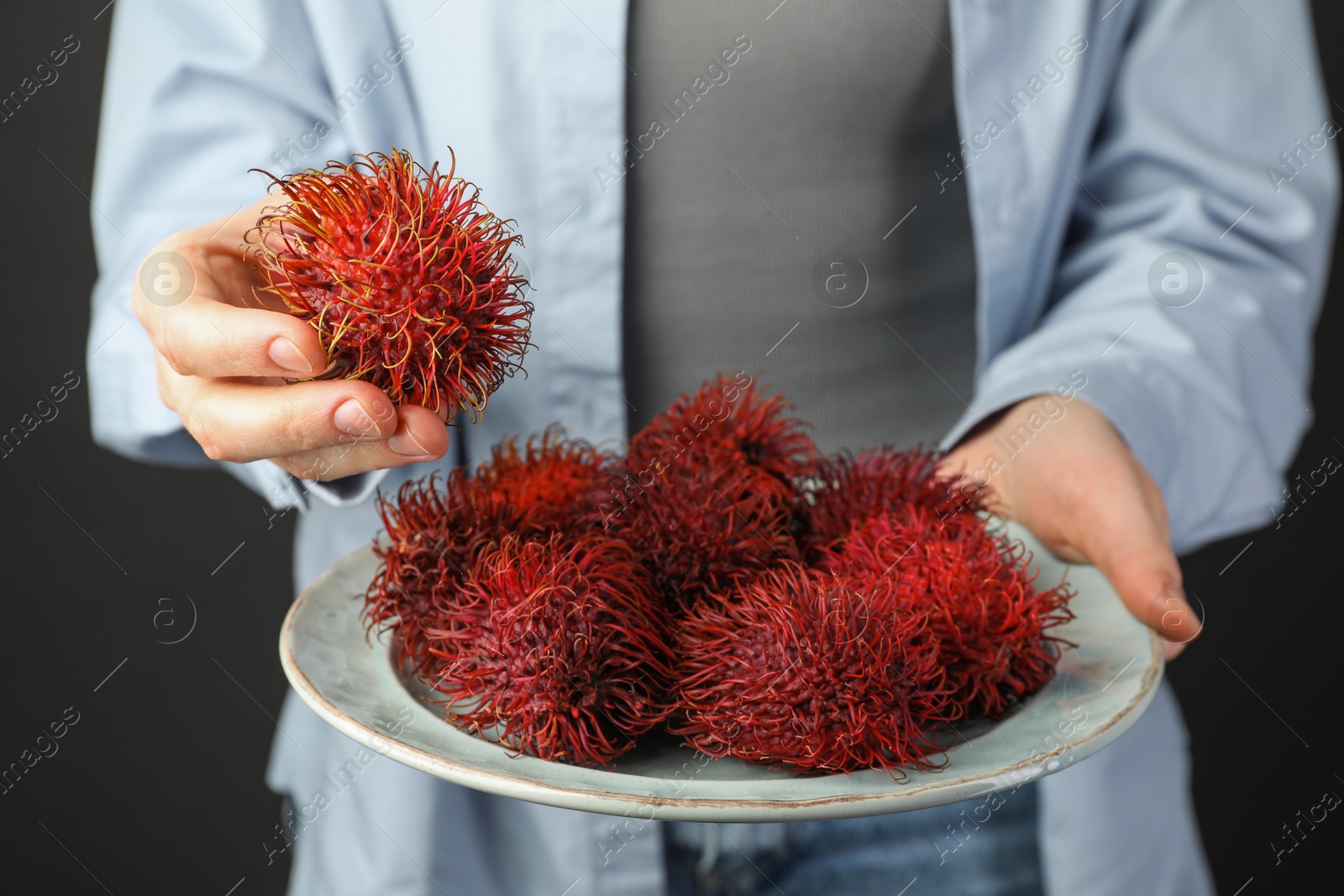 Photo of Woman holding fresh rambutans on plate against black background, closeup