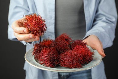 Photo of Woman holding fresh rambutans on plate against black background, closeup