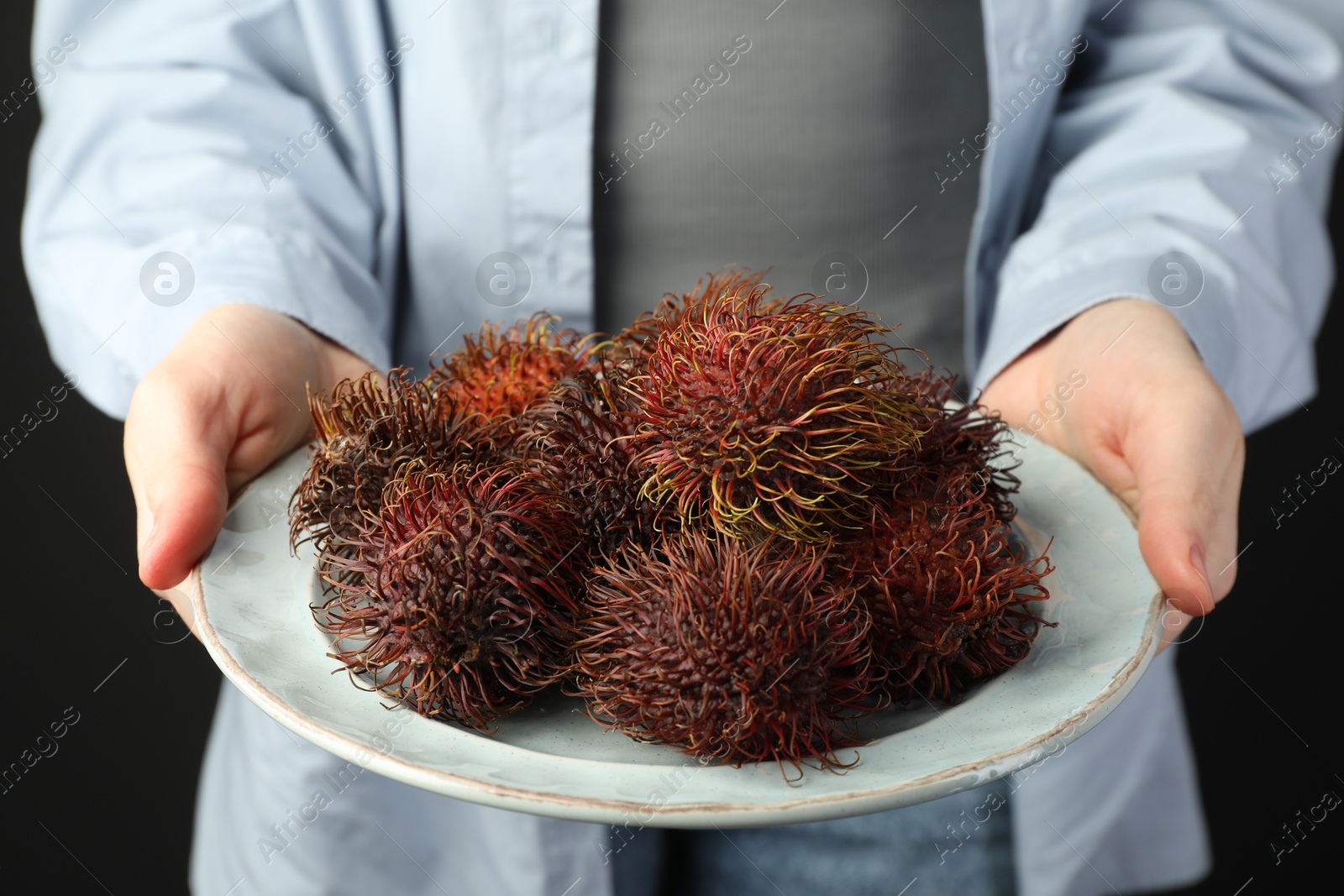 Photo of Woman holding fresh rambutans on plate against black background, closeup