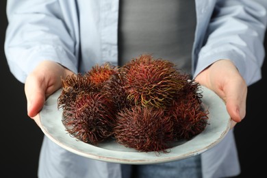 Photo of Woman holding fresh rambutans on plate against black background, closeup