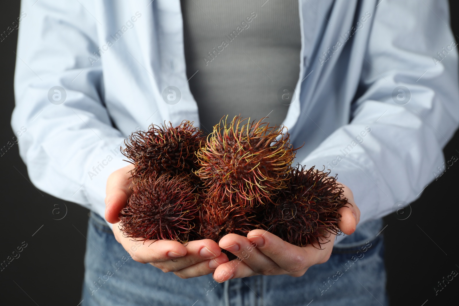 Photo of Woman holding fresh rambutans against black background, closeup