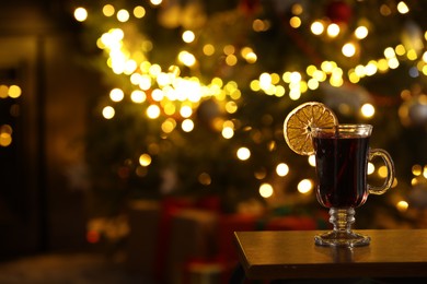 Photo of Tasty mulled wine in glass on table against blurred lights, space for text. Christmas atmosphere