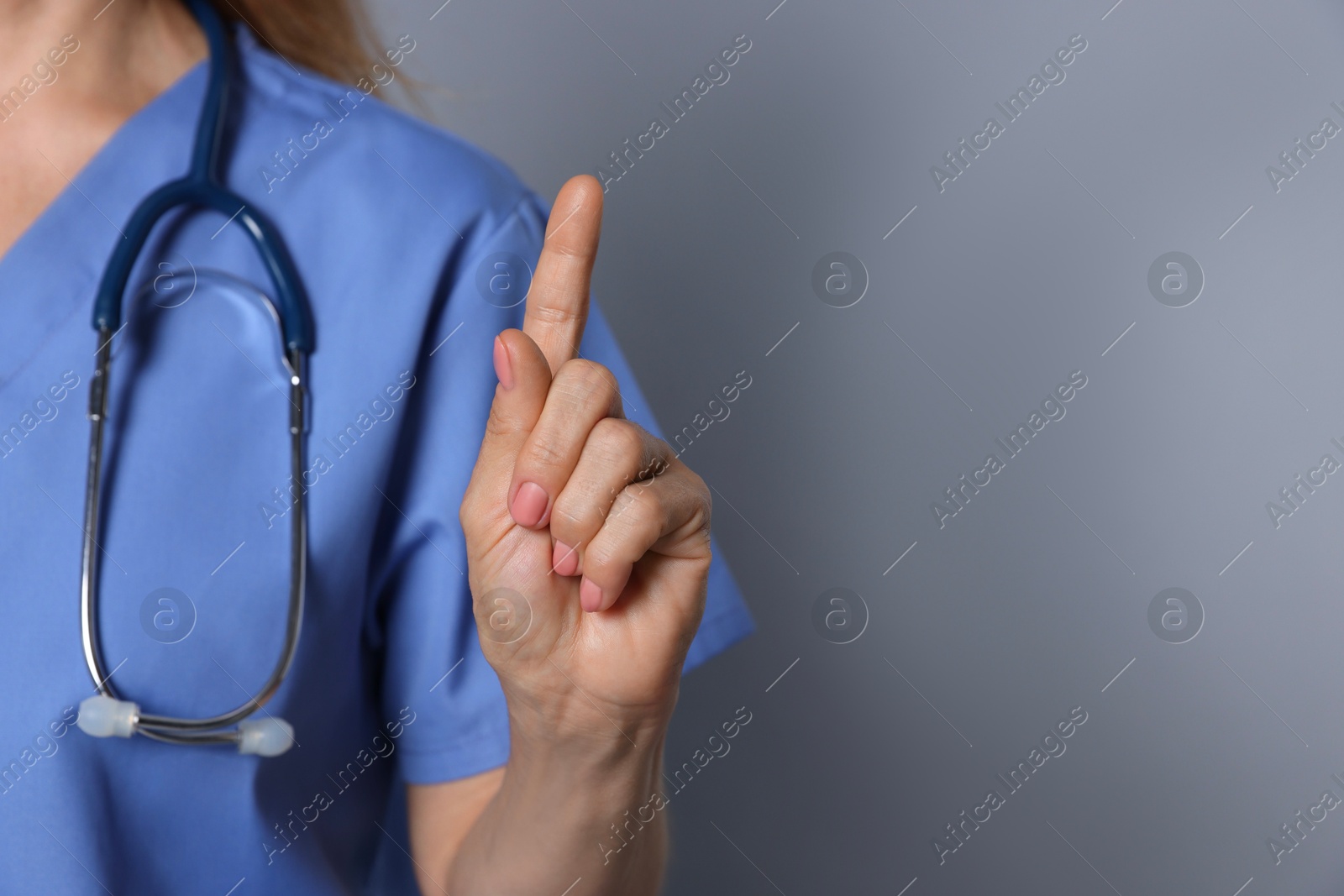 Photo of Doctor pointing at something on gray background, closeup. Space for text