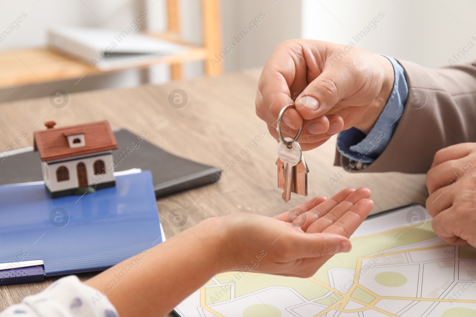 Photo of Real estate agent giving house key to new owner at wooden table, closeup