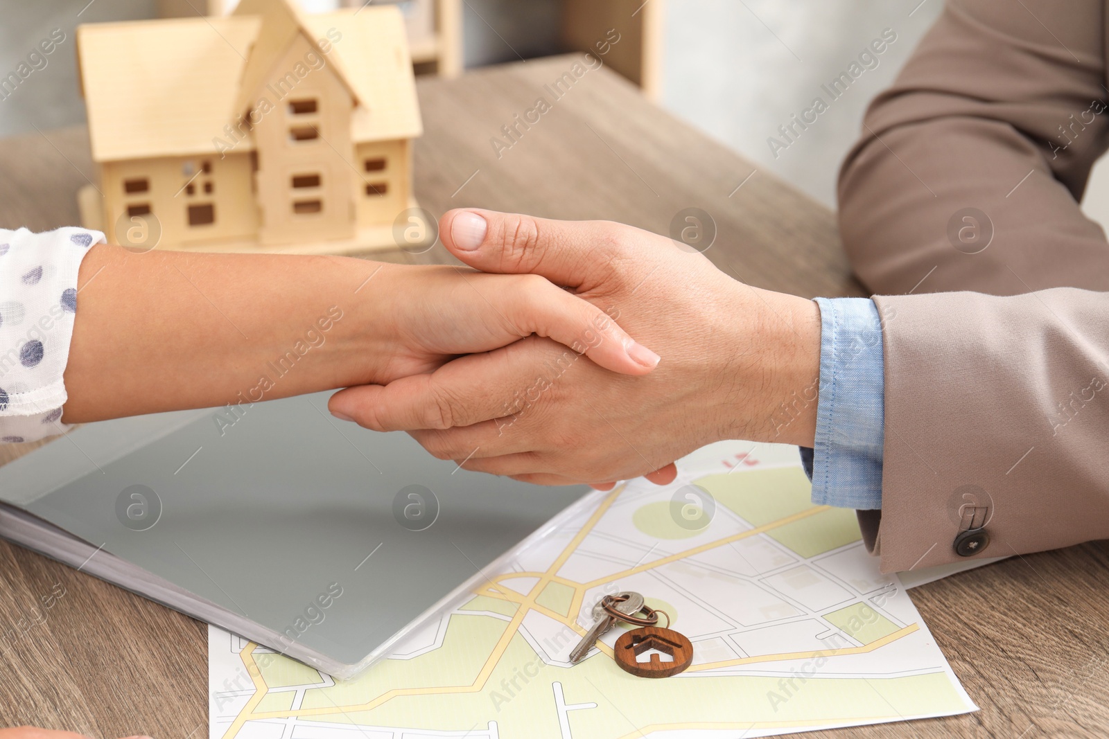 Photo of Real estate agent shaking hands with client at wooden table, closeup