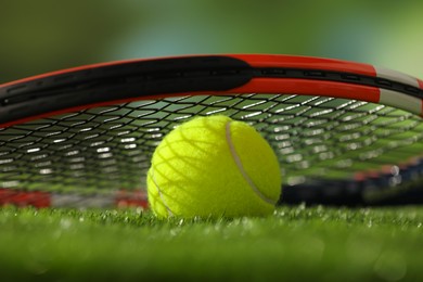 Photo of Tennis racket and ball on green artificial grass, closeup