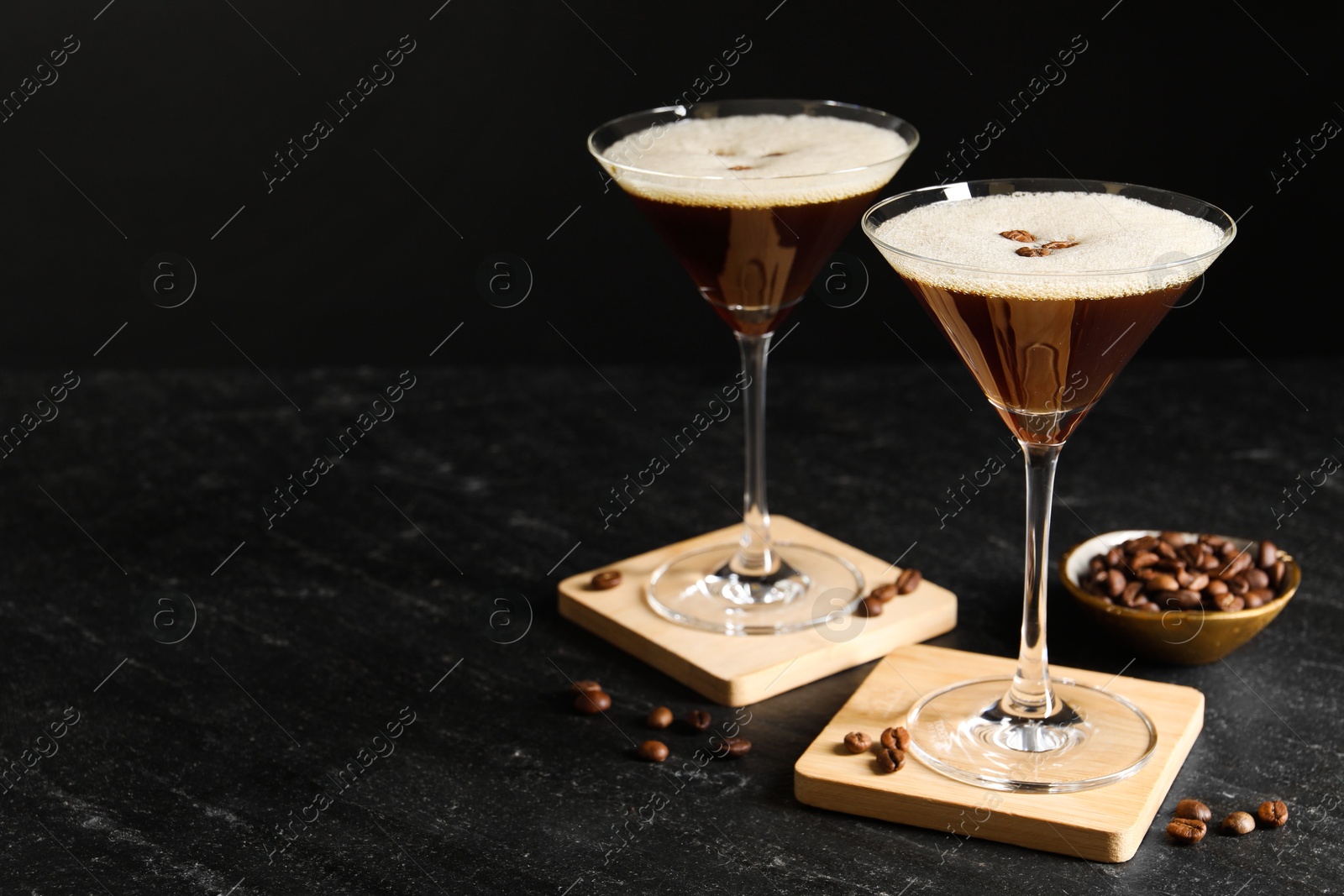 Photo of Glasses of delicious espresso martini and coffee beans on dark textured table. Space for text