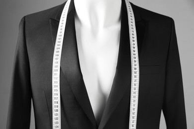 Photo of Male mannequin with black jacket and measuring tape on grey background, closeup