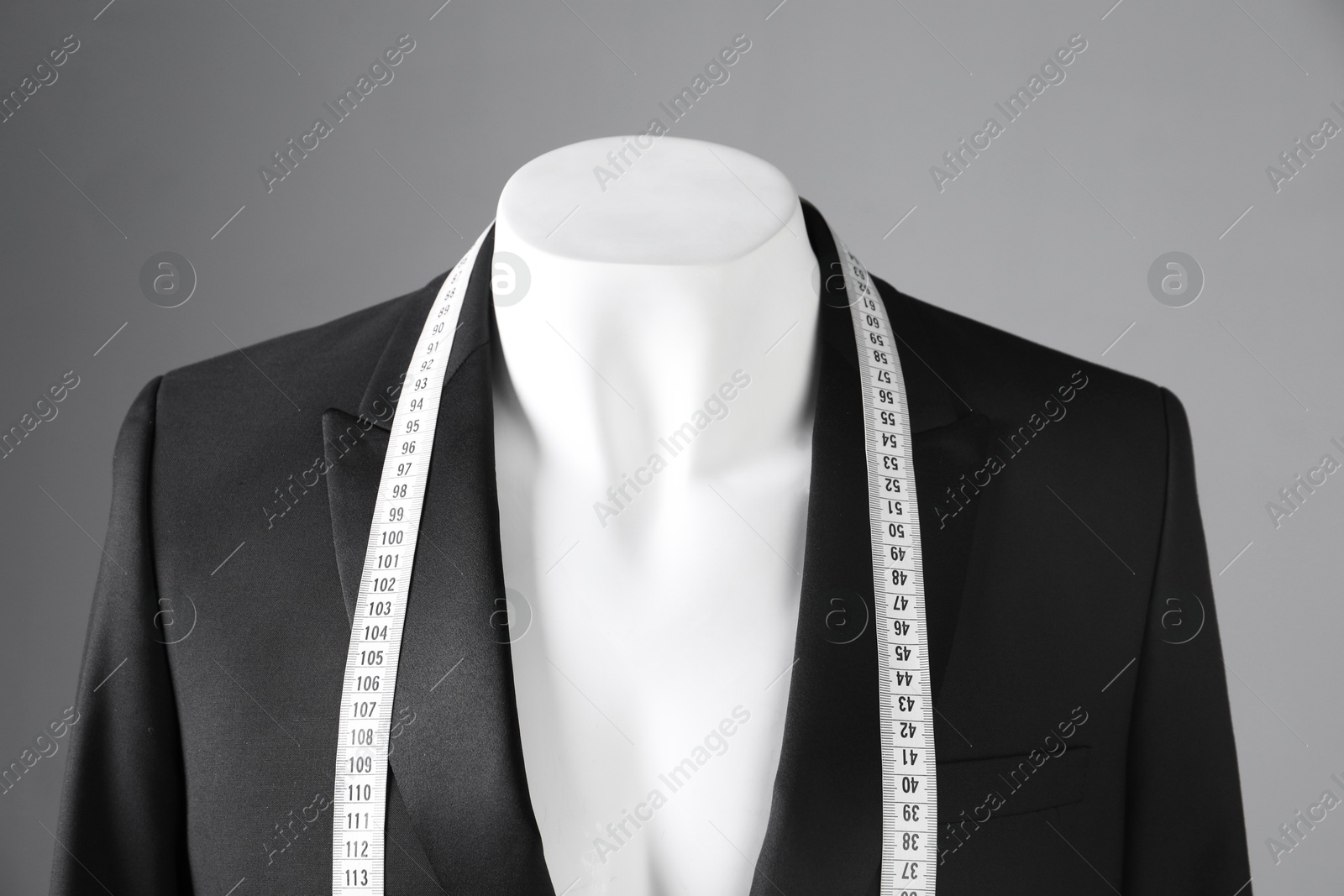 Photo of Male mannequin with black jacket and measuring tape on grey background, closeup