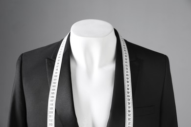 Photo of Male mannequin with black jacket and measuring tape on grey background, closeup