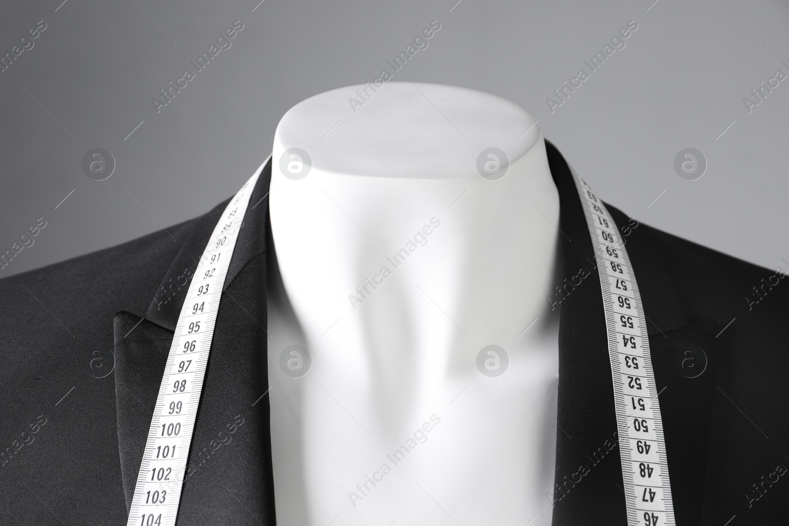 Photo of Mannequin with black jacket and measuring tape on grey background, closeup