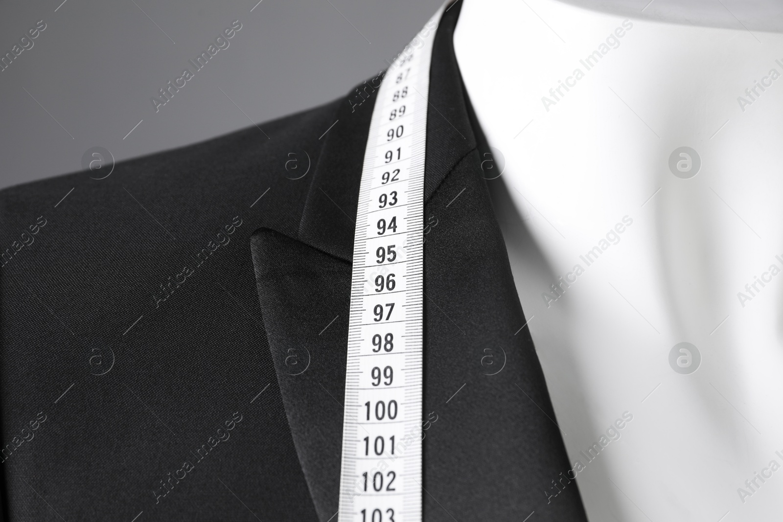 Photo of Male mannequin with black jacket and measuring tape on grey background, closeup