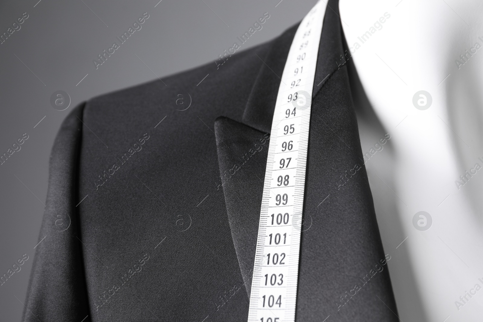 Photo of Mannequin with black jacket and measuring tape on grey background, closeup