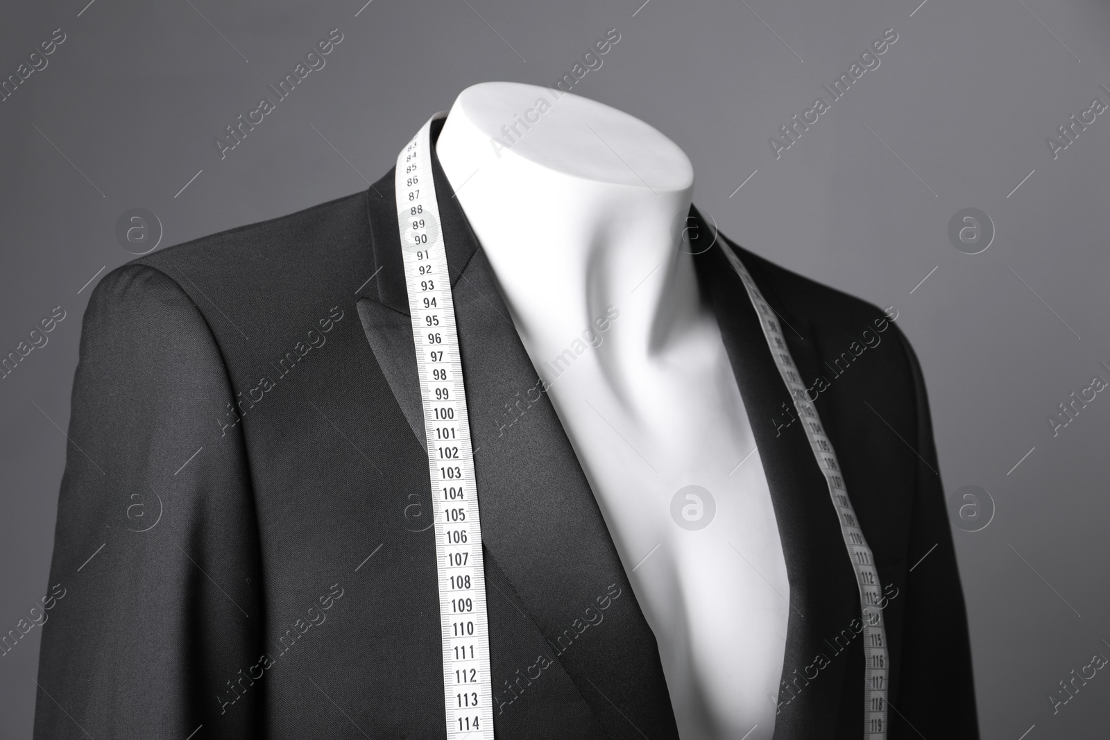 Photo of Male mannequin with black jacket and measuring tape on grey background, closeup