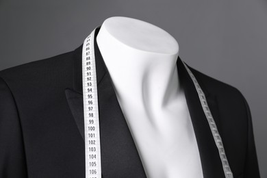 Photo of Male mannequin with black jacket and measuring tape on grey background, closeup