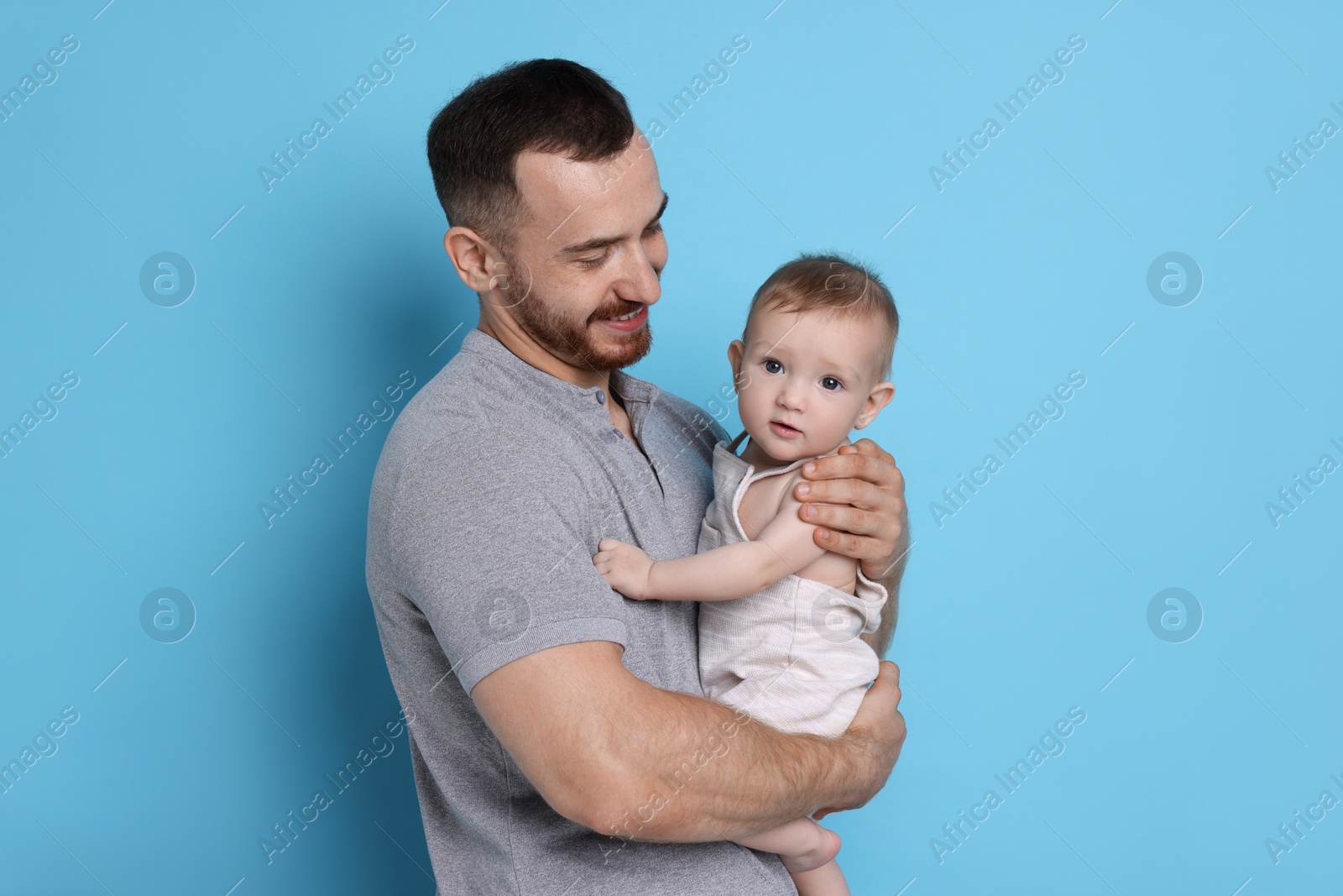 Photo of Father with his cute baby on light blue background