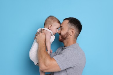 Photo of Father with his cute baby on light blue background