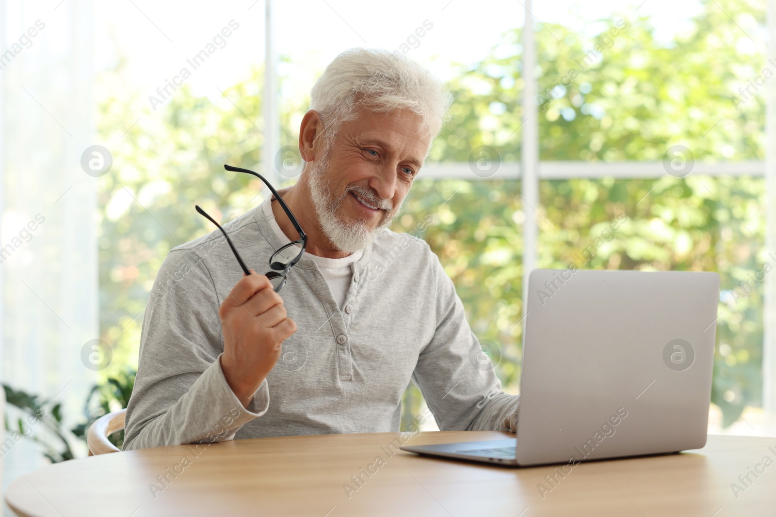 Photo of Senior man with glasses using laptop at table indoors