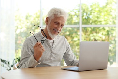 Senior man with glasses using laptop at table indoors