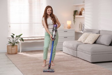 Photo of Teenage girl cleaning rug with cordless vacuum cleaner at home