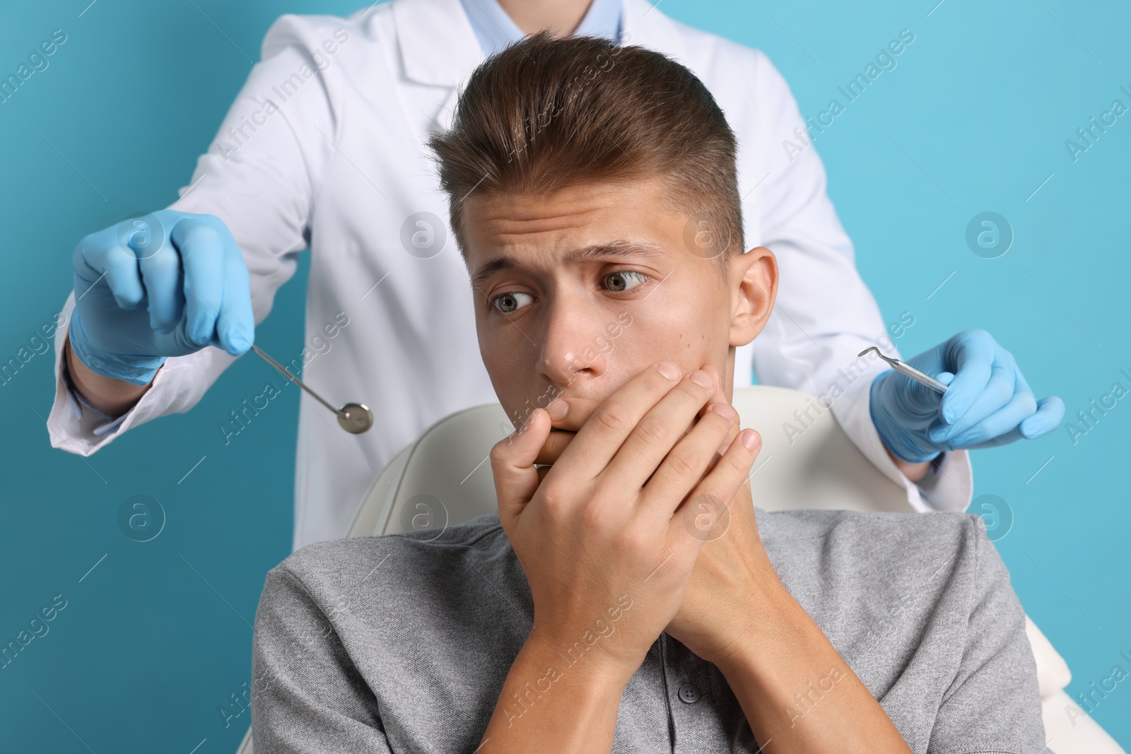 Photo of Dental phobia. Dentist working with scared man on light blue background, closeup