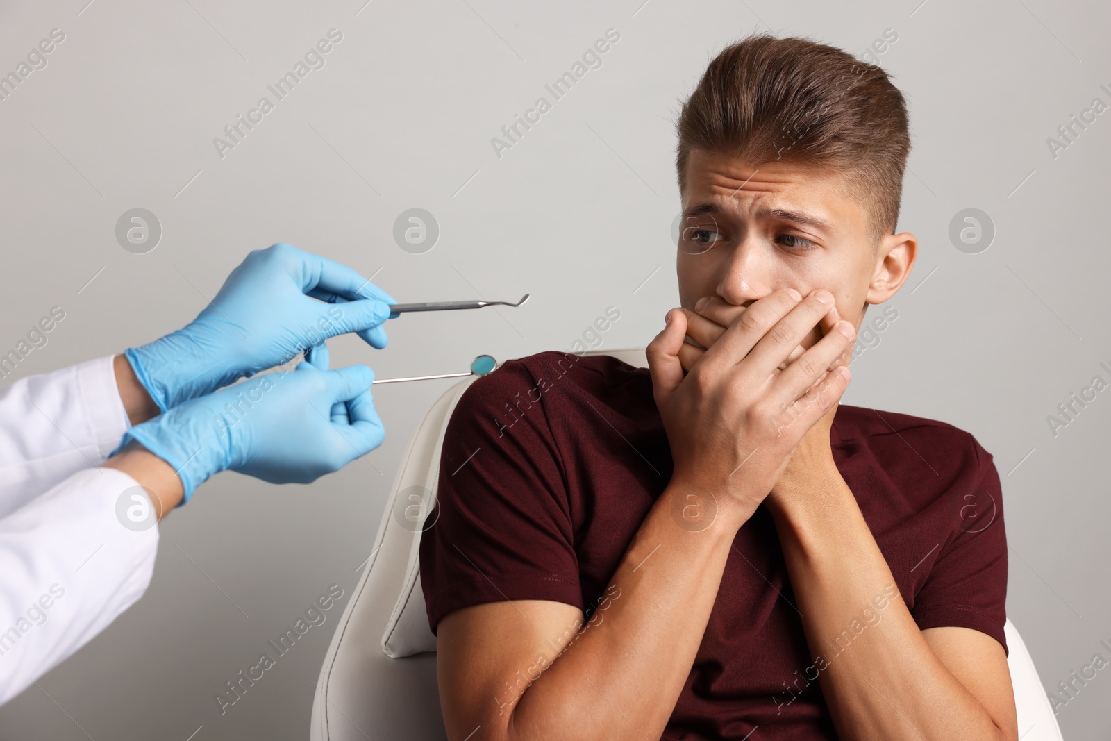 Photo of Dental phobia. Dentist working with scared man on grey background, closeup