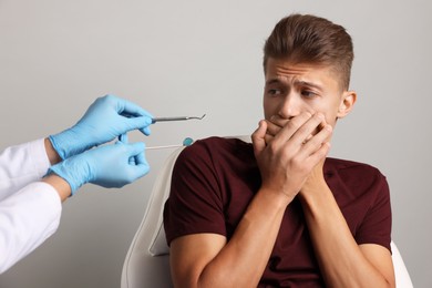 Dental phobia. Dentist working with scared man on grey background, closeup