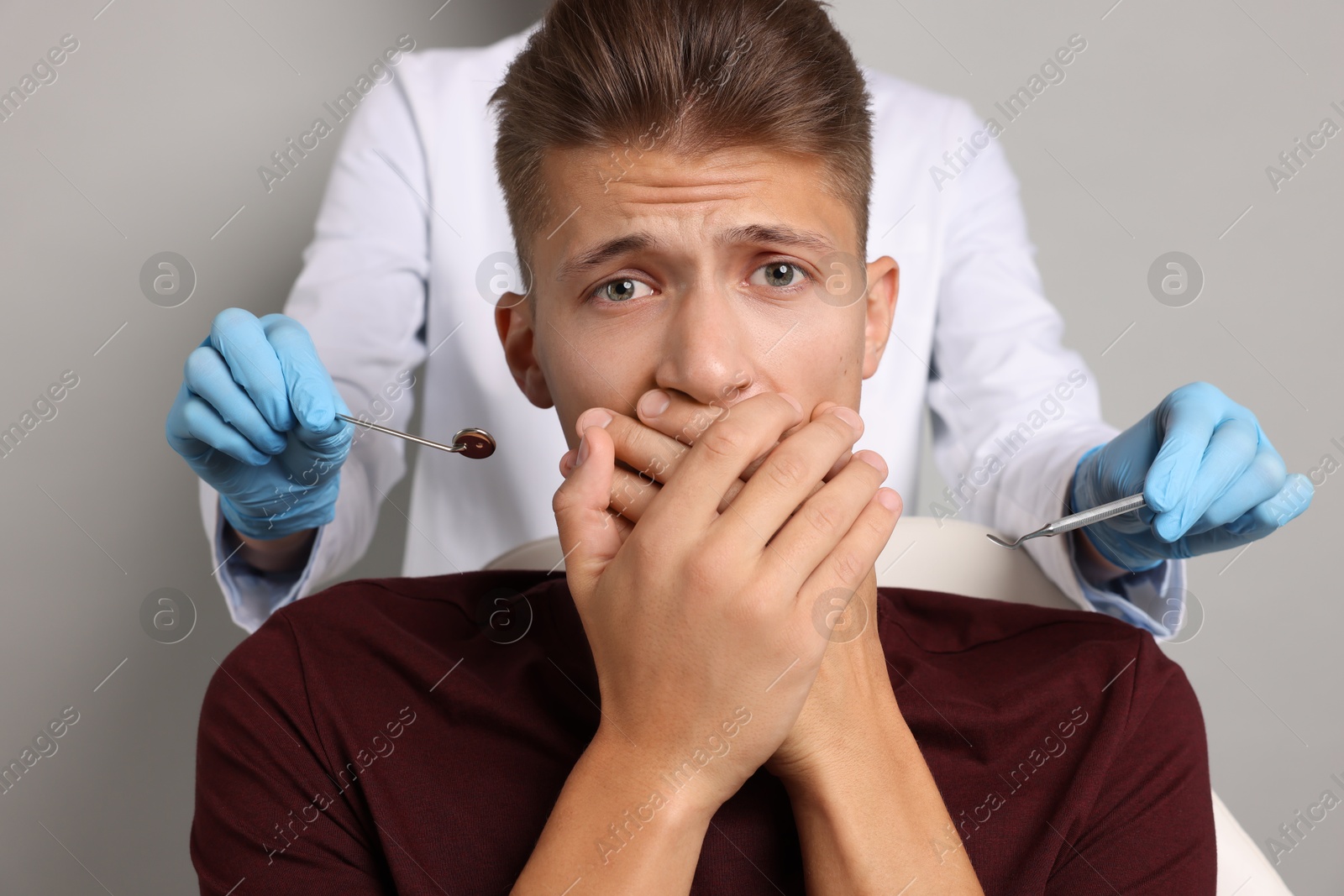 Photo of Dental phobia. Dentist working with scared man on grey background, closeup