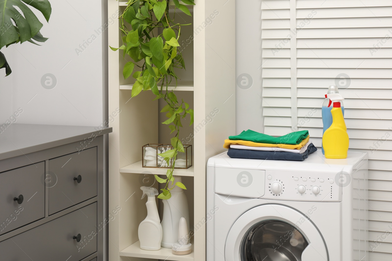 Photo of Laundry detergents and stacked clean clothes on washing machine in bathroom