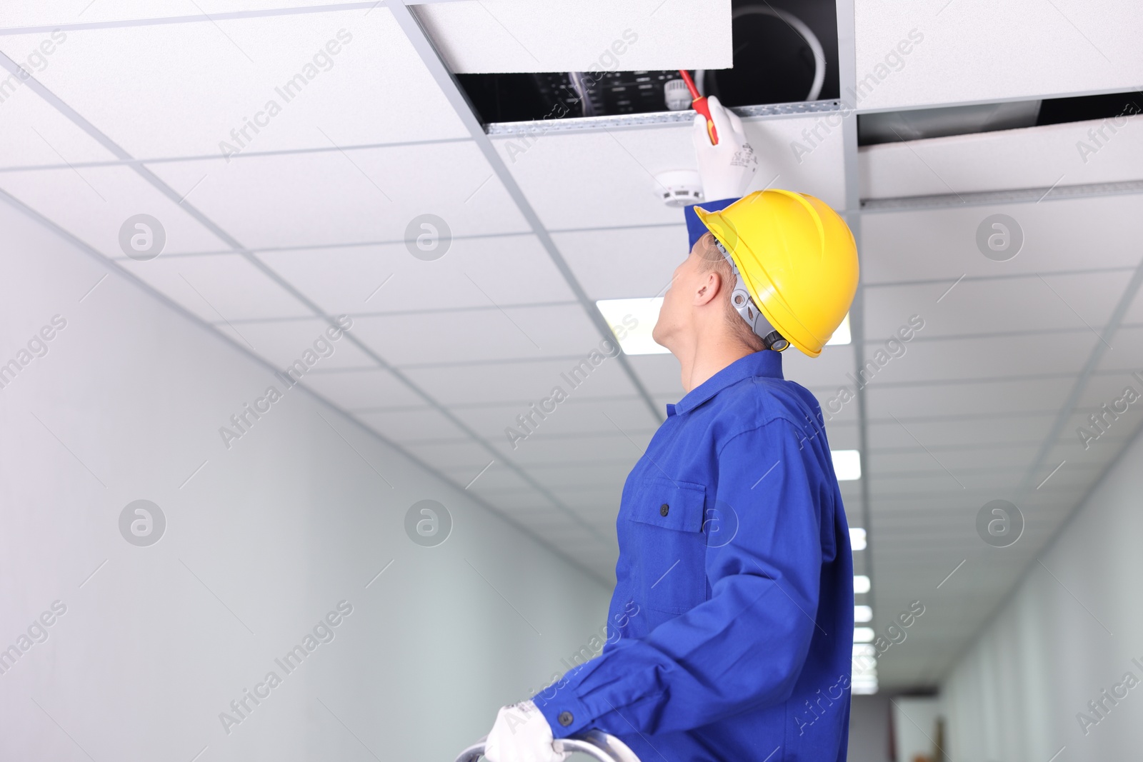 Photo of Suspended ceiling installation. Builder working with PVC tile indoors, low angle view