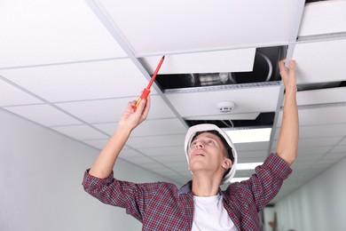 Photo of Suspended ceiling installation. Builder working with PVC tile indoors