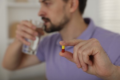 Photo of Man with pill and glass of water at home, selective focus