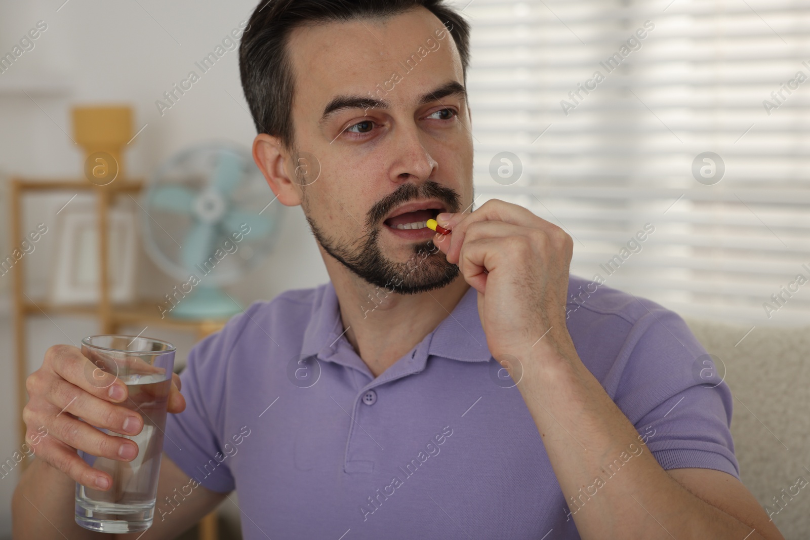 Photo of Man with glass of water taking pill at home