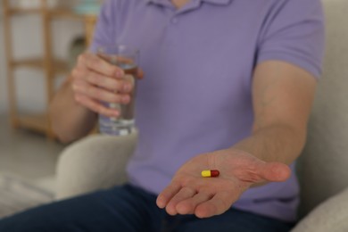 Photo of Man with pill and glass of water at home, closeup