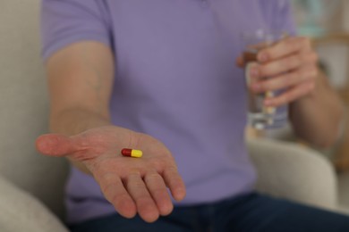 Photo of Man with pill and glass of water at home, closeup