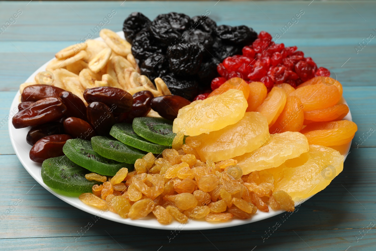 Photo of Mix of different dried fruits on light blue wooden table, closeup