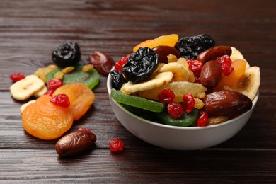 Photo of Mix of different dried fruits in bowl on wooden table, closeup