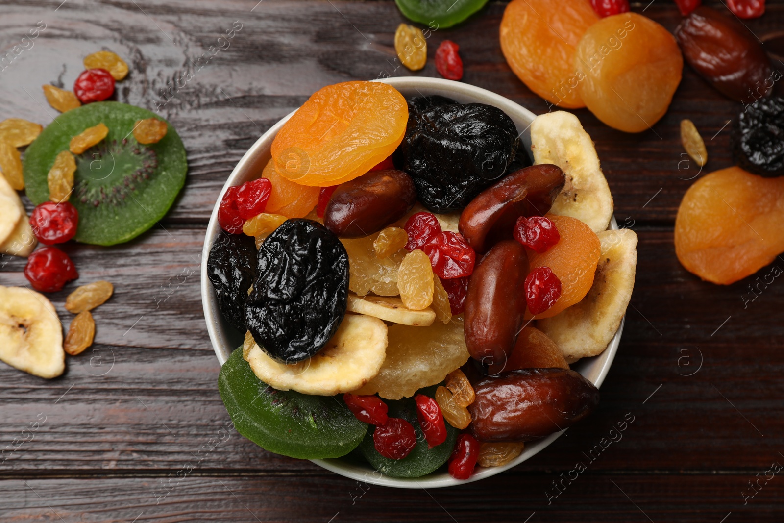 Photo of Mix of different dried fruits in bowl on wooden table, flat lay